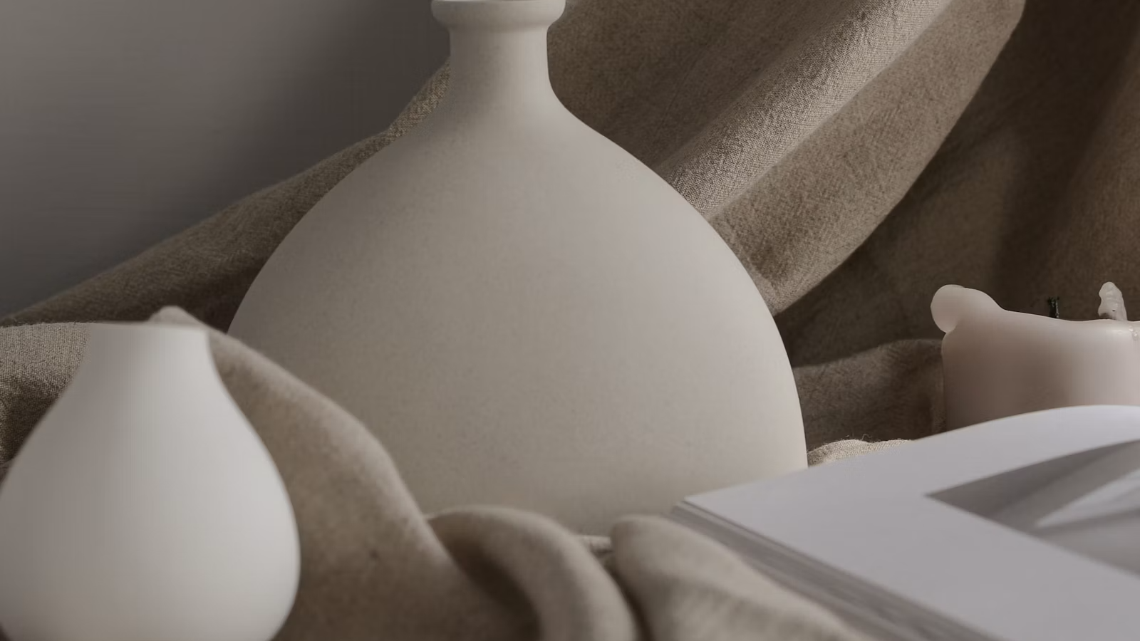 Two white ceramic vases against a plain wall, lit softly