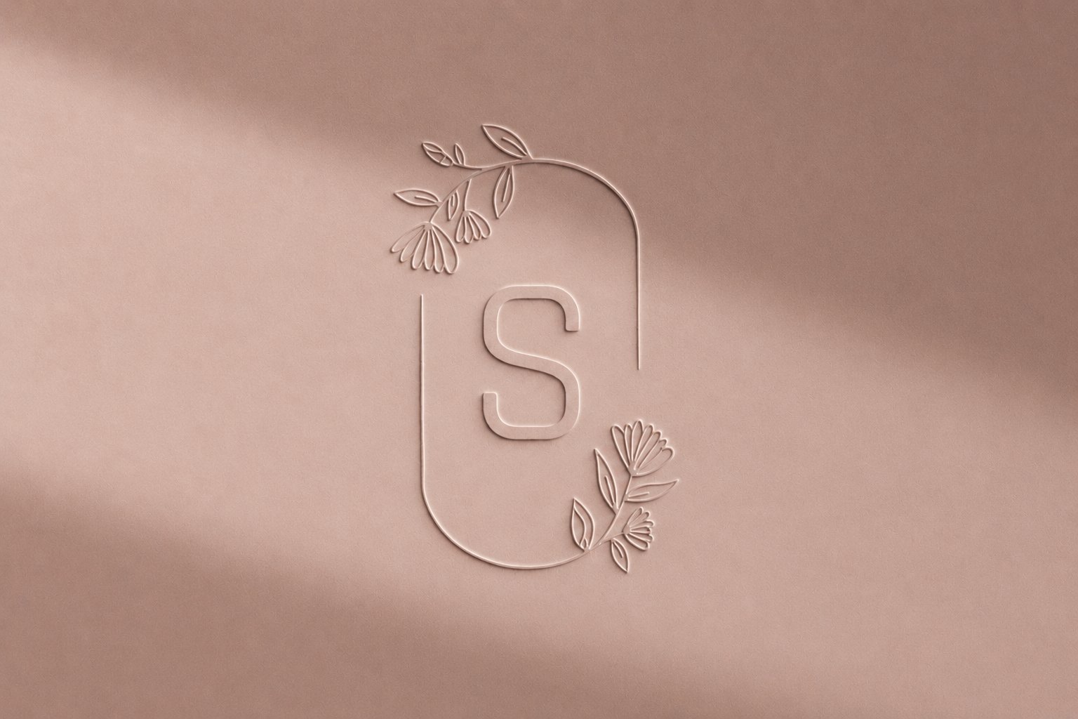 The monogram embossed into blush satin, raked light across the mark